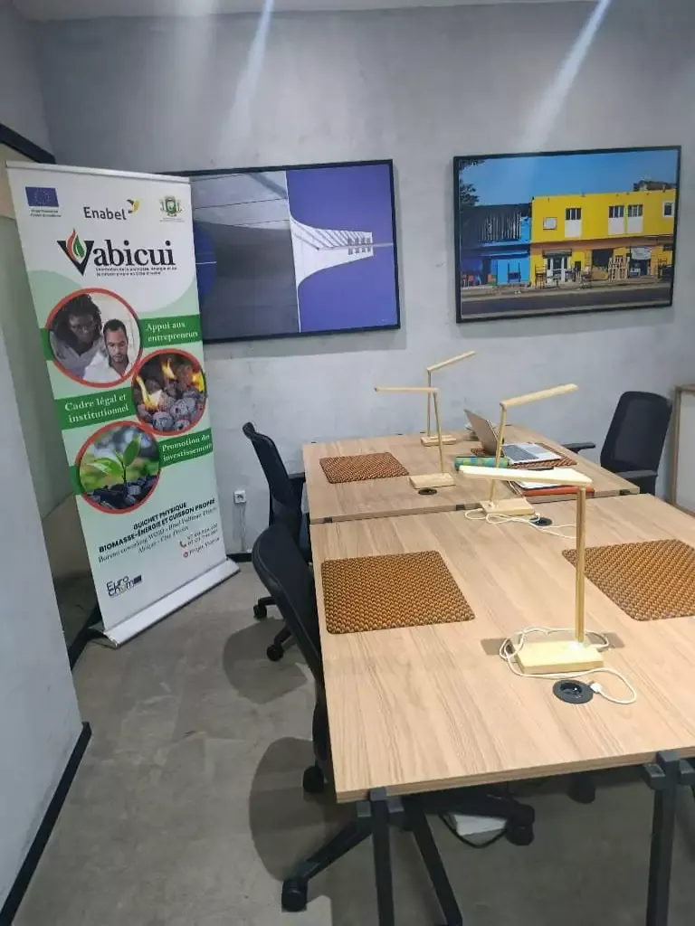 Vabicui — Salle de réunion équipée d’un bureau en bois clair avec deux chaises ergonomiques, un support pour lampe de bureau, des tapis de souris et u